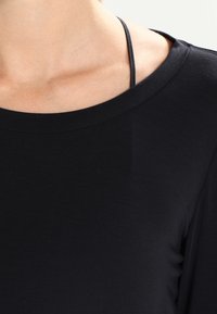 Svart långärmad topp med bred halsringning och slät textur, med en synlig tunn rem under.