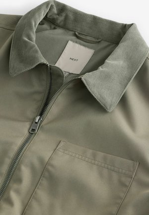Khakijacke mit Reißverschluss, Cordkragen und einer Brusttasche, aus glattem Material mit matter Oberfläche.