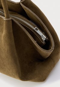 Smeđa torbica od brušene kože s glatkim patentnim zatvaračem, strukturiranim oblikom i mekom teksturom s kontrastnim kožnim obrubom.