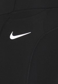 Mustat urheiluleggingsit, joissa on litteät saumat, sileä pinta ja suuri valkoinen Nike-tikkun logo edessä.