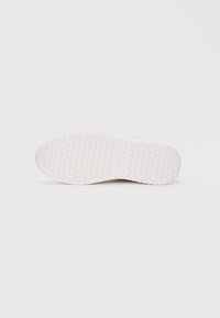White rubber shoe sole with a textured, patterned grip, featuring small circular indents and defined edges for durability and traction.