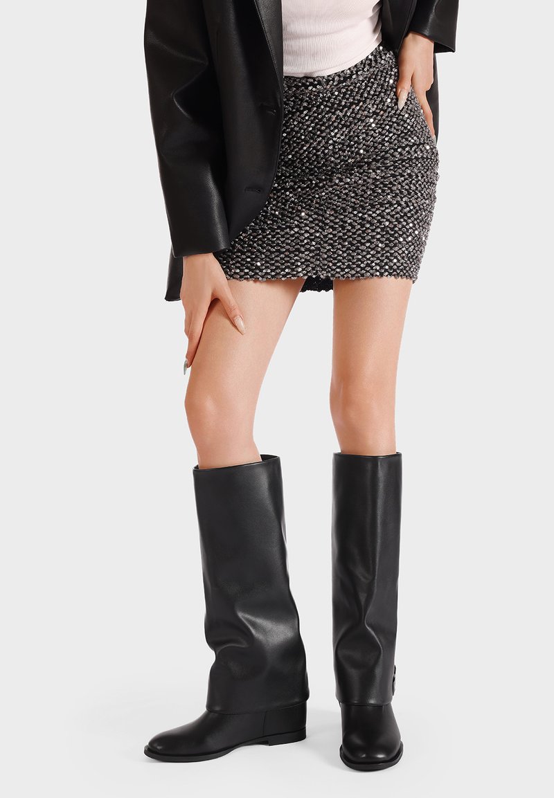 Botas de cuero negras hasta la rodilla con un diseño suelto, combinadas con una falda mini texturizada y brillante. Silueta limpia y moderna con un acabado elegante.
