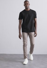Sort tekstureret t-shirt med korte ærmer parret med beige slim-fit bukser og hvide sneakers. Simple design, glat stof og minimal accent.