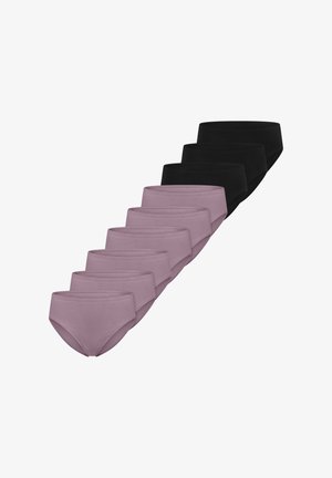 Vrouw met schouderlang krullend haar, gekleed in een zwarte beha en bijpassende zwarte slip met hoge taille tegen een effen achtergrond.