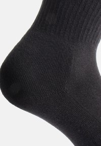 Calcetín de algodón negro con textura acanalada, punta redondeada y talón reforzado, mostrando un fino detalle de punto.