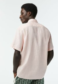 Vaaleanpunainen lyhythihainen paita, jossa on pellavamainen rakenne. Ominaisuuksiin kuuluu klassinen kaulus ja slim fit -malli. Yhdistetty kuvioituihin vihreisiin shortseihin.