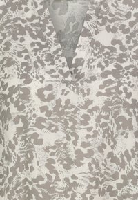 V-Ausschnitt-Bluse aus hellbeigem Stoff mit einem grauen Animal-Print-Muster. Weiche Textur mit fließendem Fall und subtiler Schimmer.