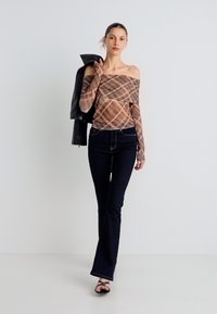 Top estampado con hombros descubiertos en tonos beige y marrón, combinado con jeans azules oscuros acampanados y sandalias negras de tiras. Chaqueta de cuero negra en mano.