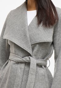 Szary płaszcz z wełny o szerokim kołnierzu, zapinany na krzyż, z paskiem do wiązania, z pionowymi szwami i miękką teksturą.