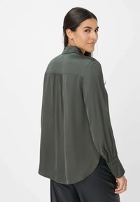 Camicia a maniche lunghe di colore verde scuro, realizzata in tessuto morbido, con colletto, pieghe posteriori e polsini con bottoni; orlo arrotondato.