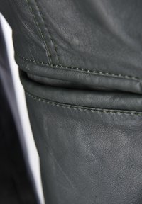 Mörkgrön läder med en slät textur. Har framträdande sömmar i en kontrasterande färg nära en vikt sektion.