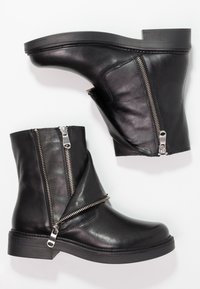 Czarne skórzane botki za kostkę z okrągłym noskiem, z ukośnymi zamkami błyskawicznymi i niskim obcasem. Widoczna gładka tekstura oraz minimalne przeszycia.