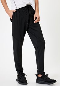 Sorte atletiske joggers lavet af letvægts, strækbart stof. Funktioner inkluderer et elastisk taljebånd, snøre og tapered manchetter.