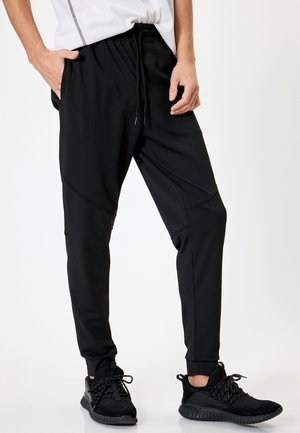 Pantalones deportivos negros fabricados con un tejido ligero y elástico. Incluyen cinturilla elástica, cordón ajustable y puños ajustados.