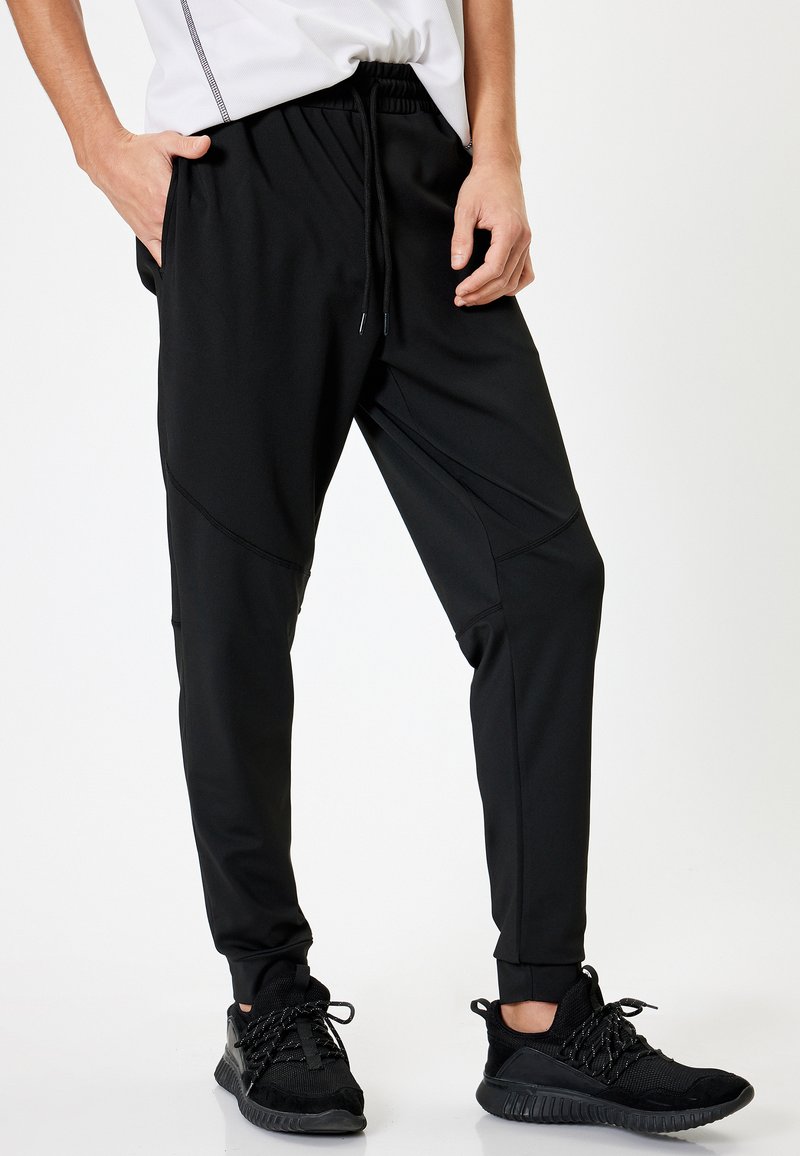Sorte atletiske joggers lavet af letvægts, strækbart stof. Funktioner inkluderer et elastisk taljebånd, snøre og tapered manchetter.
