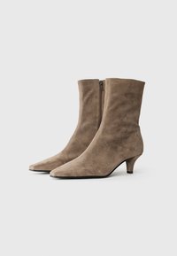 Bottines en daim taupe avec un bout pointu et un talon de 3 cm. Elles sont dotées d'une fermeture zippée sur le côté et d'une texture lisse.