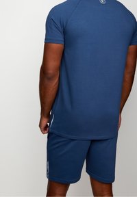 T-shirt de sport bleu marine à manches raglan courtes, associé à un short assorti avec des rayures blanches sur les côtés. Tissu en coton mélangé doux.