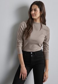 Ribbelige, tan kleurige lange mouw top met een hoge halslijn, gecombineerd met hooggesneden zwarte jeans met twee knopen aan de voorkant en zijzakken.
