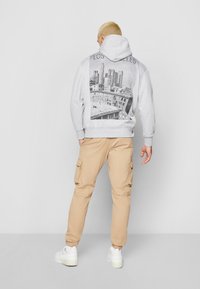 Felpa grigia con una stampa grafica di Los Angeles sulla schiena, abbinata a pantaloni cargo beige. Il materiale sembra morbido e presenta una vestibilità rilassata.