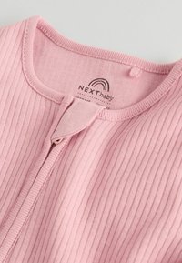 Ružový rebrovaný detský odev s okrúhlym výstrihom, zapínaním na patentky vpredu a štítkom s logom "NEXT baby". Mäkká bavlnená textúra.