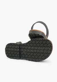 Sole di sandalo in gomma nera con un motivo testurizzato, dotata di un plantare in sughero marrone e dettagli della cinghia abbinati. Design completamente piatto e forma flessibile.