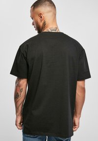 Svart kortermet t-skjorte med rund hals, laget av bomull. Har et ensfarget design, glatt tekstur, og en litt lengre bakhem.