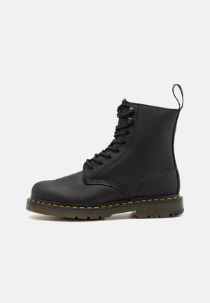 Schwarze Leder-Ankle-Boots mit Schnürung vorne, gelben Nähten, runder Spitze, Gummisohle und einem Ziehschlaufen hinten. Glatte Textur.
