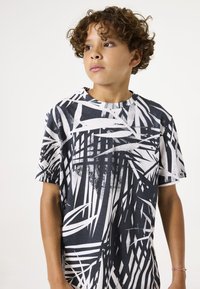Schwarzes und weißes T-Shirt mit kurzem Arm und geometrischem Blattmuster. Weicher Baumwollstoff und Rundhalsausschnitt. Lässige Passform.
