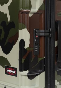Svart och grön kamouflagemönstrad hårdskalsresväska med kombinationslås, texturerad yta, dragkedjor och en Eastpak-logotyp på sidan.