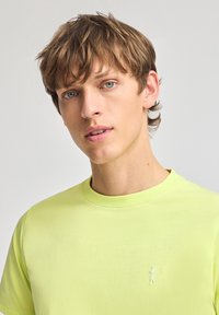 Ljusgrön t-shirt med rund halsringning, gjord av mjuk bomull, med en liten, broderad golfare-logotyp på bröstet och korta ärmar.