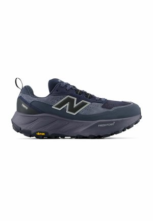Mørkeblå trail løbesko med tyk sål, trækstrop ved hælen, New Balance-logo og "Fresh Foam" og "Vibram" branding på sålen.