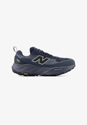 Dunkelblauer Trailrunning-Schuh mit dicker Sohle, Zuglasche an der Ferse, New Balance Logo und "Fresh Foam" sowie "Vibram" Branding auf der Sohle.