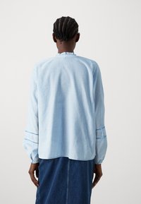 Blusa a righe blu chiaro con maniche lunghe, scollatura arricciata e polsini elasticizzati, che presenta un tessuto morbido e una vestibilità comoda.