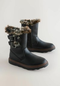Zwarte faux leren laarzen met een met bont gevoerde boord, voorzien van twee zilveren gespen en een gestructureerde rubberen zool. Ritssluiting voor gemakkelijke aan- en uittrekken.