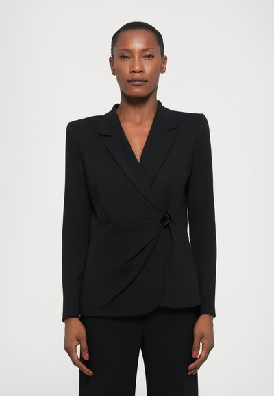 Černý blazer vyrobený z hladké látky s překládkovým designem a klopovým límcem. Obsahuje dekorativní černou sponu v pase a dlouhé rukávy.