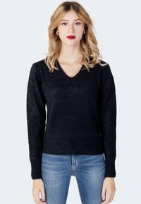 Pulover negru cu decolteu în V, realizat dintr-un tricot texturat, având mâneci lungi și o siluetă ajustată. Asortat cu blugi de un albastru deschis.
