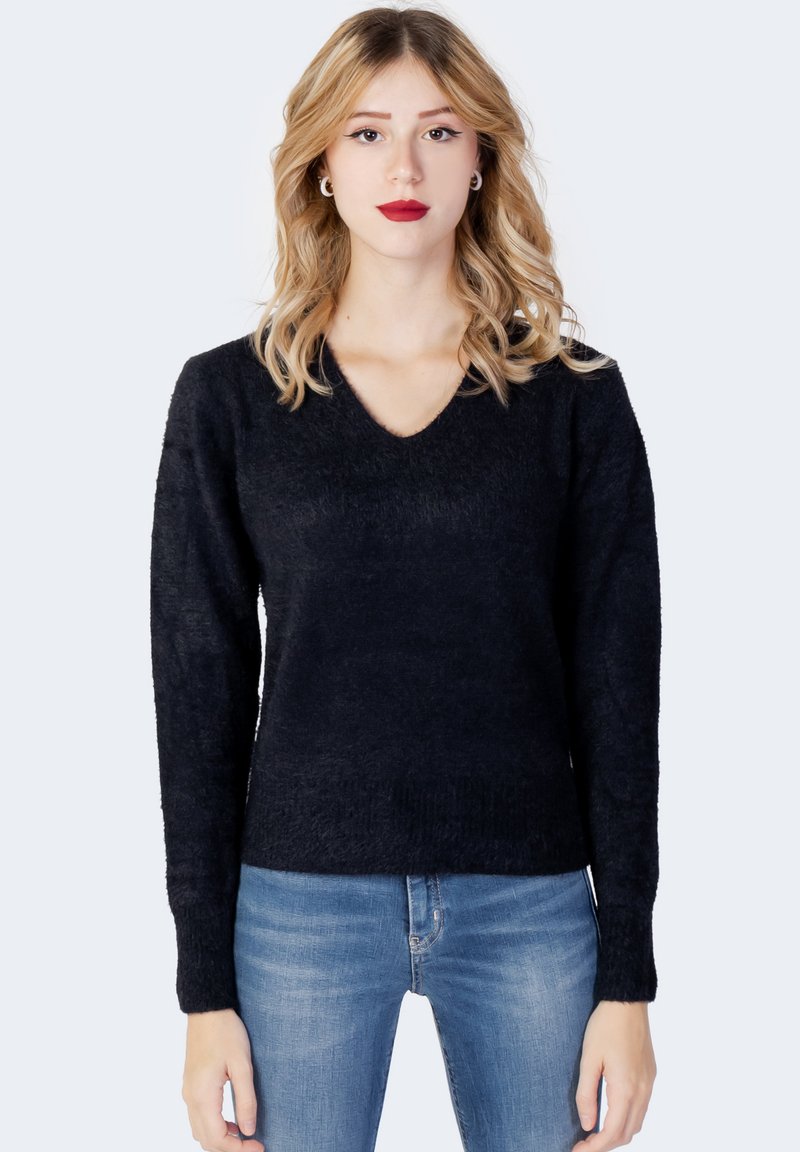 Pulover negru cu decolteu în V, realizat dintr-un tricot texturat, având mâneci lungi și o siluetă ajustată. Asortat cu blugi de un albastru deschis.