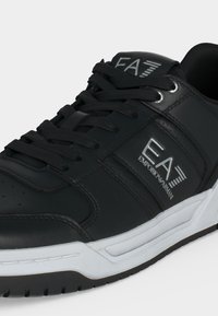 Baskets en cuir noir avec lacets noirs, semelle blanche et logo argenté Emporio Armani EA7 sur le côté et la languette.
