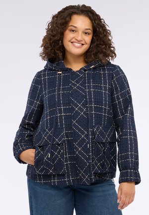 Giacca a vento blu navy con texture trapuntata, presenta un motivo a quadri in fili bianchi e dorati, e due tasche frontali.