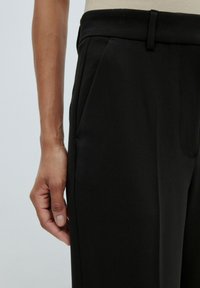 Zwarte broek met een tailored ontwerp, een soepele textuur, zijzakken en een platte voorkant. Hand ligt op de zijnaad voor schaal.