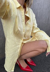 Chemise en lin jaune avec des manches longues et une poche poitrine, assortie à des escarpins rouges à bout pointu. Tissu texturé et coupe décontractée.