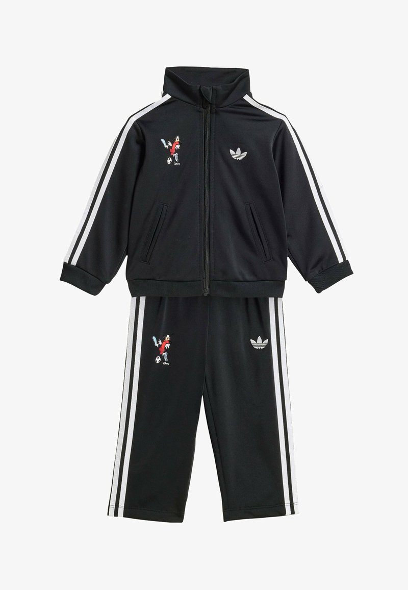 Zwarte Adidas trainingspak met witte strepen, jas met rits, broek, en een geborduurd plaatje van Mickey Mouse die voetbal speelt op zowel jas als broek.