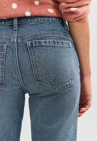 Ljusblå högmidjade jeans med en klassisk femficksdesign, som har bruna sömmar och en lätt blekt textur.