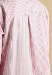 Vue arrière d'une chemise rose avec des rayures verticales vertes et fines bleues et un pli creux central sous un empiècement chevrons.