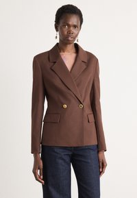 Brun dobbeltspent blazer laget av teksturert stoff, med en skarp krage, to frontlommer og detaljer med gullfargede knapper.