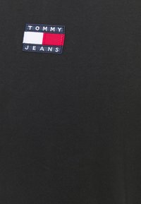 Černé bavlněné tričko s obdélníkovým vyšitým logem v tmavě modré, bílé a červené barvě s nápisem "TOMMY JEANS." Jednoduchý a přiléhavý design.