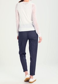 Vit stickad tröja med spetsärmar, kombinerad med marinblå rutiga byxor och vita sneakers. Enkel, avslappnad passform.