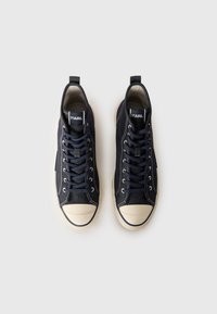 Høye sneakers i marineblå canvas med en beige gummitåkappe, snøring foran og merkevarelogo på tungen og siden. Teksturert stoffoverflate.