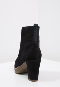 Czarne zamszowe botki za kostkę na grubej podeszwie; mają tylną pętelkę do zakupu oraz subtelne detale przeszycia. Gładka tekstura i zaokrąglony nosek.