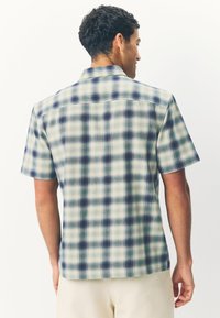 Short-sleeve plaid shirt featuring a blend of green, blue, and white colors. The fabric has a smooth texture with a classic collar design.